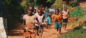 CHEZA children running and walking on brown sand surrounded with trees during daytime